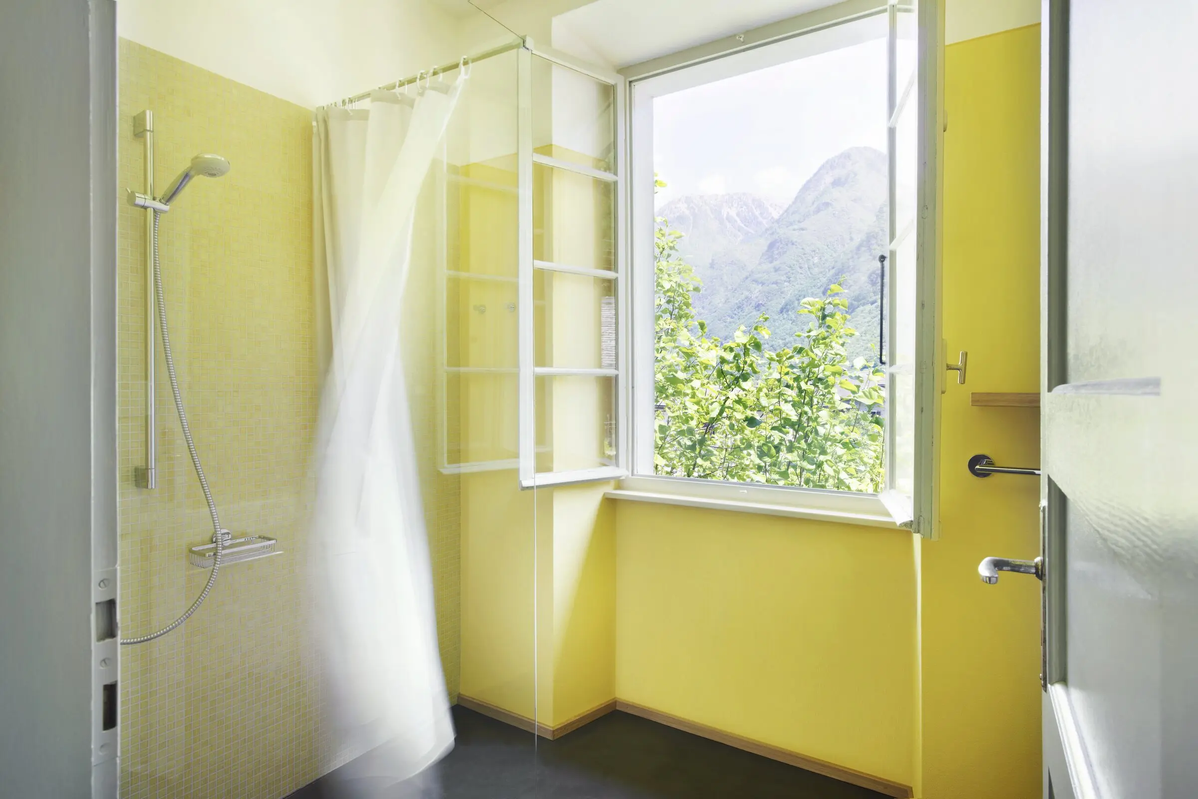 Gelb gefliestes Badezimmer mit Dusche und offenem Fenster zum Bergpanorama