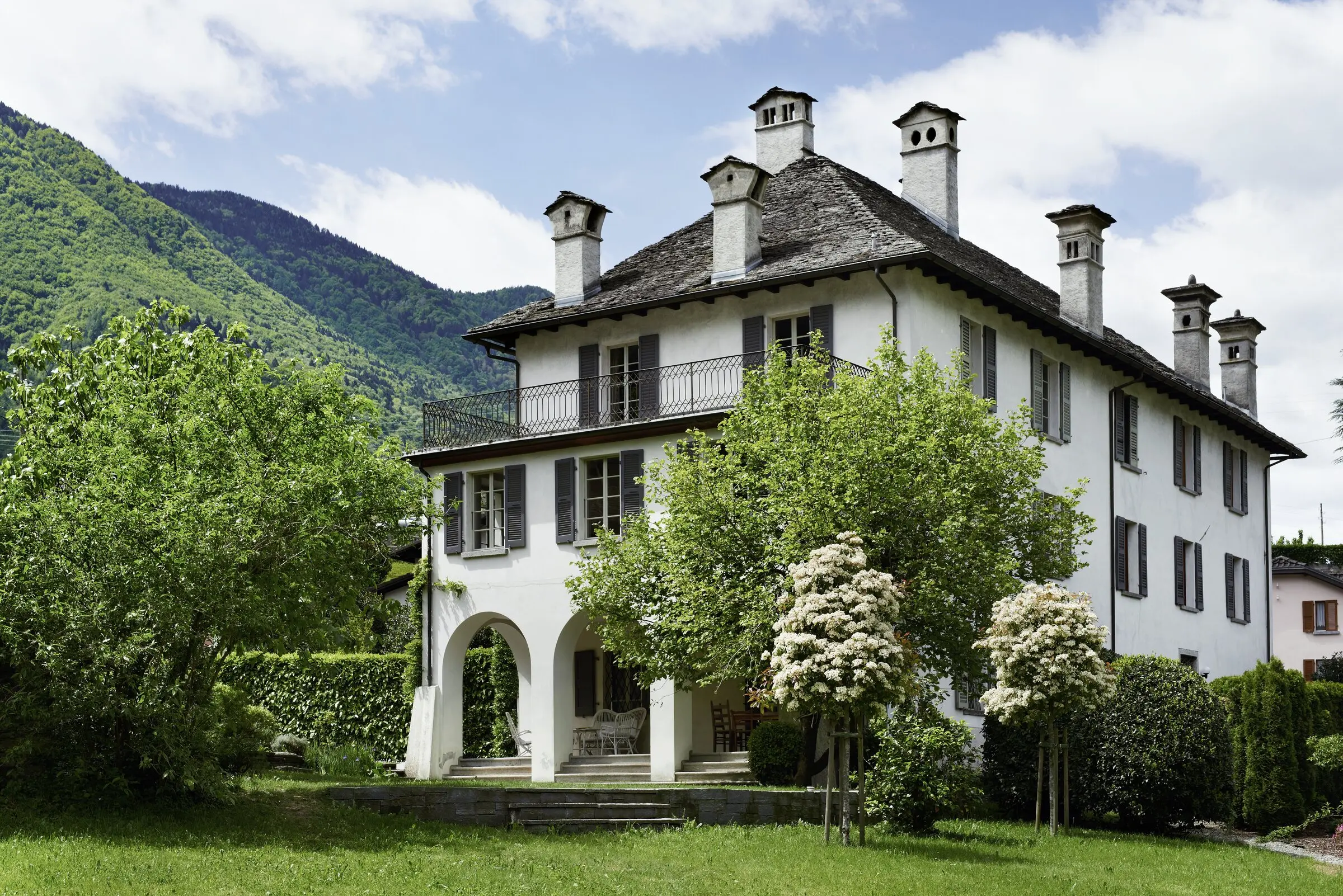 Frontansicht von Toveda mit Arkadengang, flankiert von blühenden Bäumen