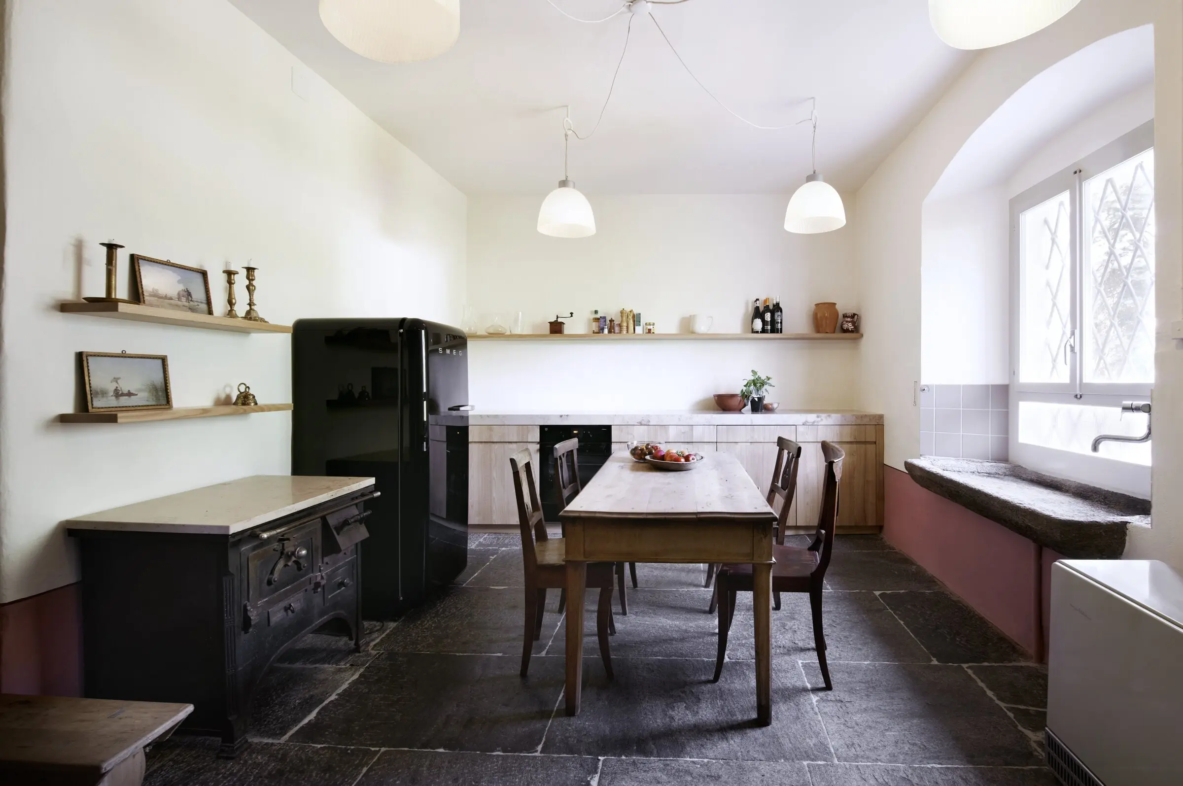 Küche mit langem Esstisch, schwarzem Ofen und Kühlschrank auf Steinboden
