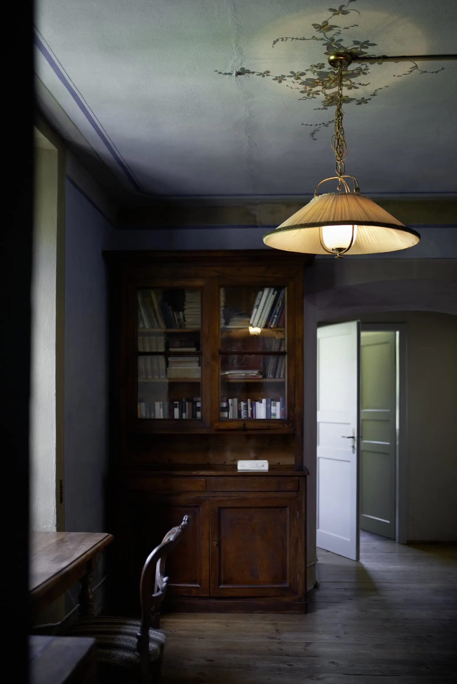 Salon mit antikem Bücherschrank und Hängelampe unter verzierter Stuckdecke